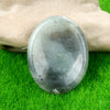 A smooth, oval gray natural crystal stone massage tool resting on bright green grass.