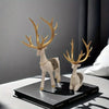 A set of two resin deer figurines with golden antlers and gold accents displayed on a dark box.