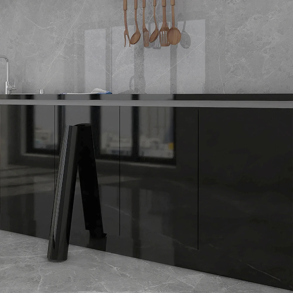 A modern kitchen countertop with a black slab and dark cabinetry, featuring a marble peel-and-stick backsplash film above.