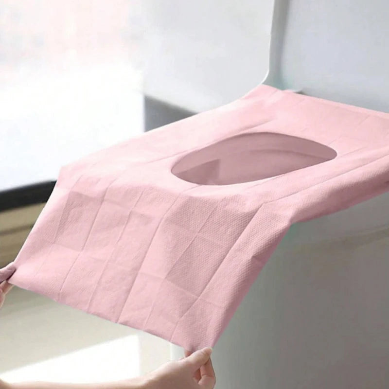 A pink disposable toilet seat cover is shown being placed on a toilet, demonstrating its fit and design.