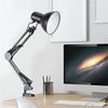 A black adjustable swing arm desk lamp is positioned next to a computer monitor on a wooden desk.