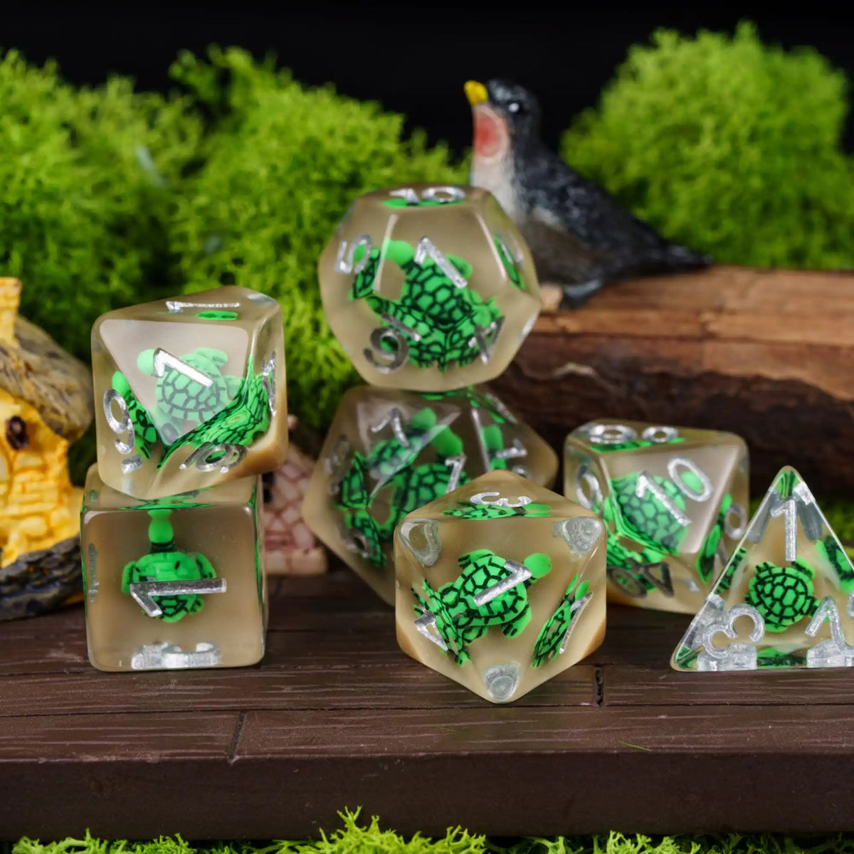 A set of adorable animal resin dice featuring green and black designs, displayed on a wooden surface with greenery in the bac