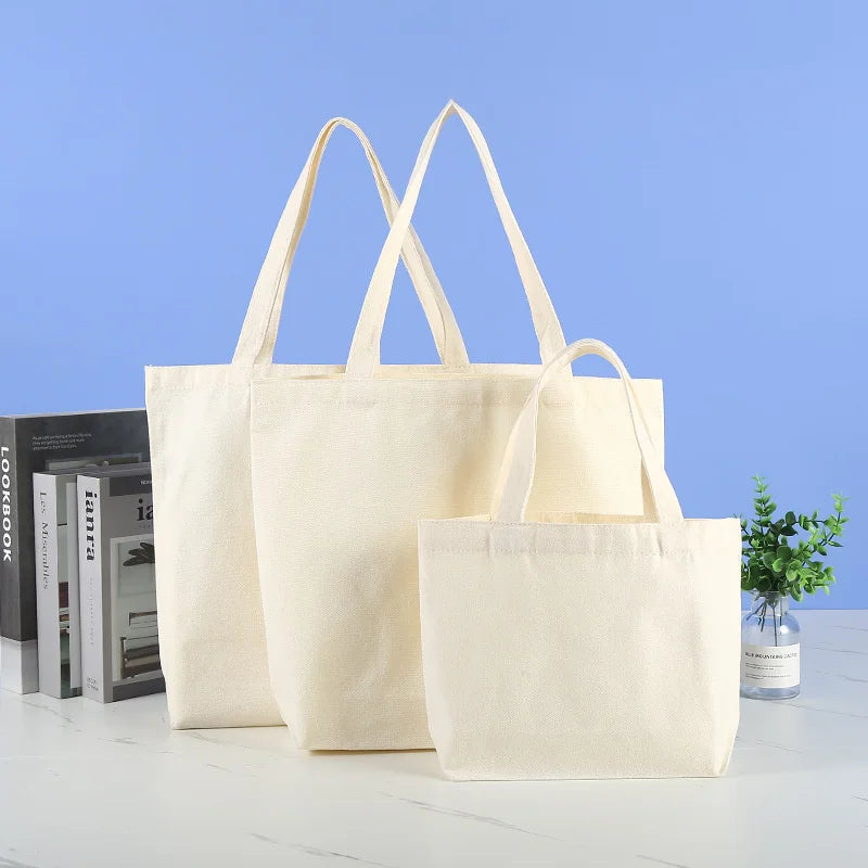 Three natural canvas shopping tote bags are displayed against a light blue background.