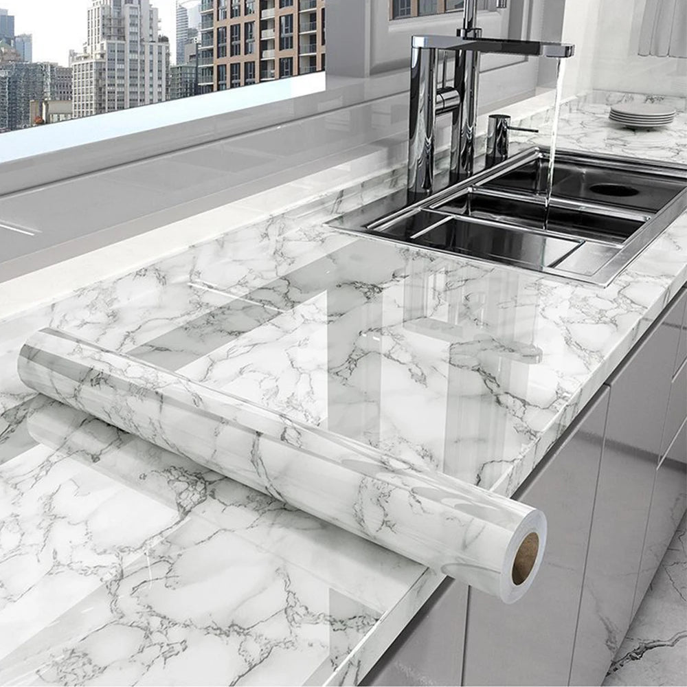 A marble peel-and-stick film is shown rolled out on a white marble countertop next to a kitchen sink.