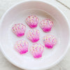 Pink iridescent seashell resin charms scattered in a white bowl