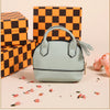 A light mint green compact PU leather earbud case with a black trim and a tassel keychain, placed on a surface next to checke