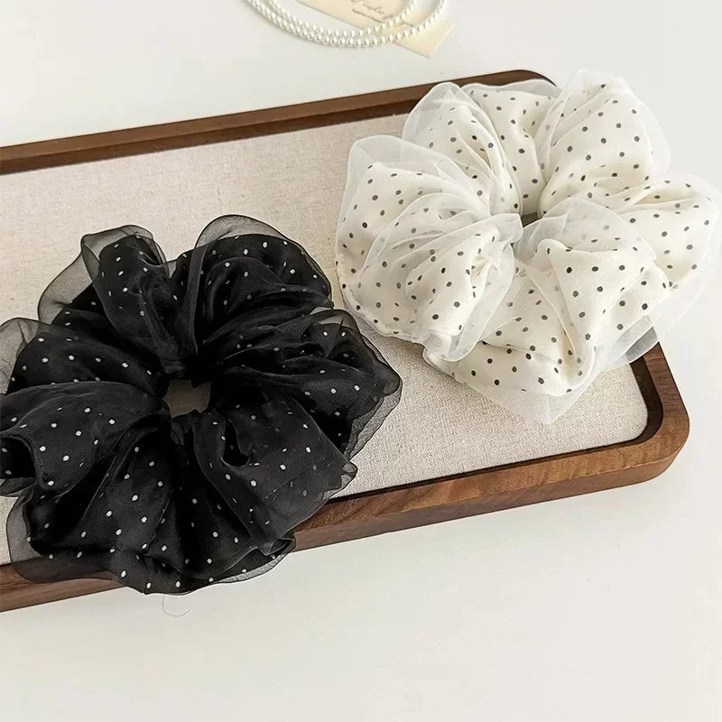 A pair of black polka dot mesh scrunchie hair ties and a white polka dot fabric scrunchie displayed on a wooden tray.