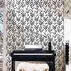A piano is placed in front of a white brick wall covered with black and white leaf peel-and-stick wallpaper.