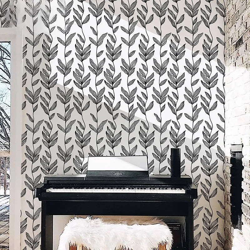 A piano is placed in front of a white brick wall covered with black and white leaf peel-and-stick wallpaper.
