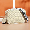 A beige and black compact crossbody bag with a white pattern and black strap resting on a light surface.