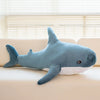 Weiches blaues riesiges Haifisch-Plüschtier auf einem hellen Sofa neben einem Fenster.