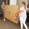 A woman is using orange furniture moving straps to secure a large cardboard box for moving.