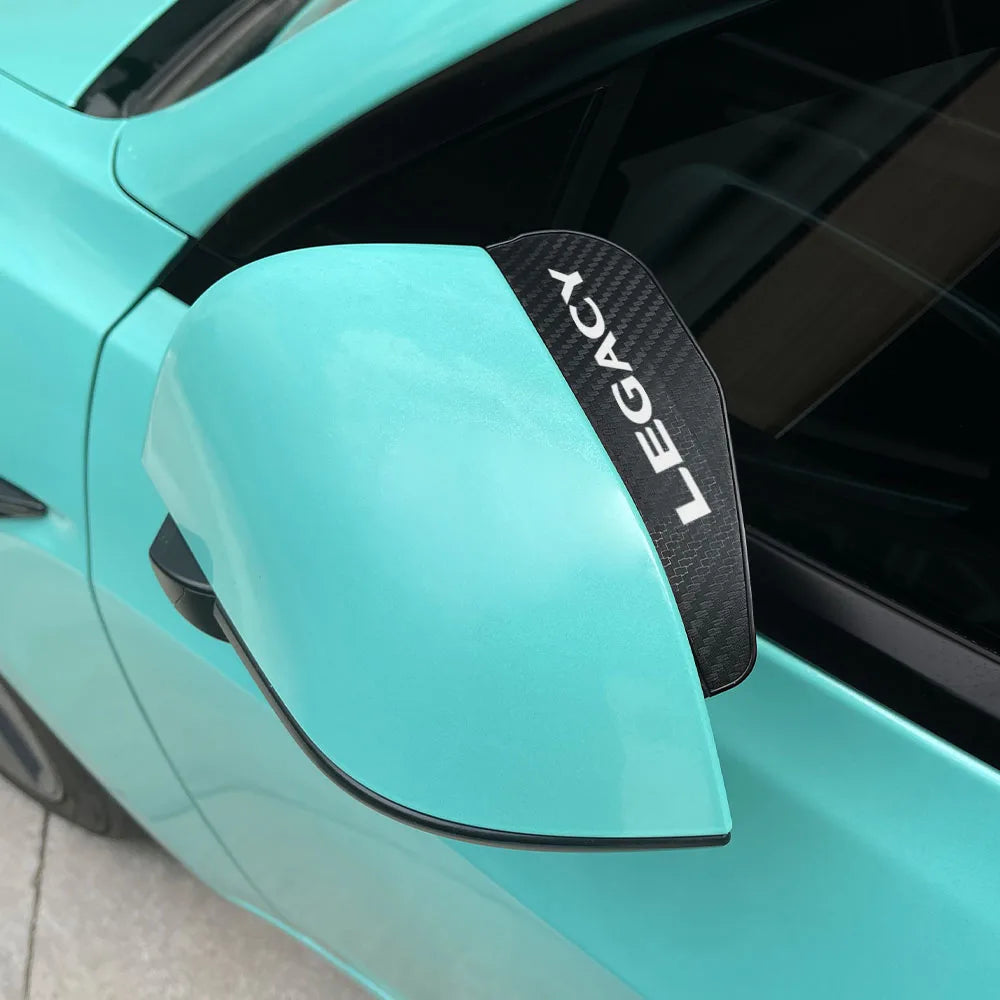 A close-up of a teal Subaru rain guard mirror visor with black lettering that reads LEGACY.
