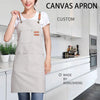 A woman wearing a light beige canvas apron with large front pockets in a kitchen setting.