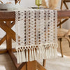 Beige bohemian farmhouse tasseled table runner with intricate crochet detailing on a wooden table.