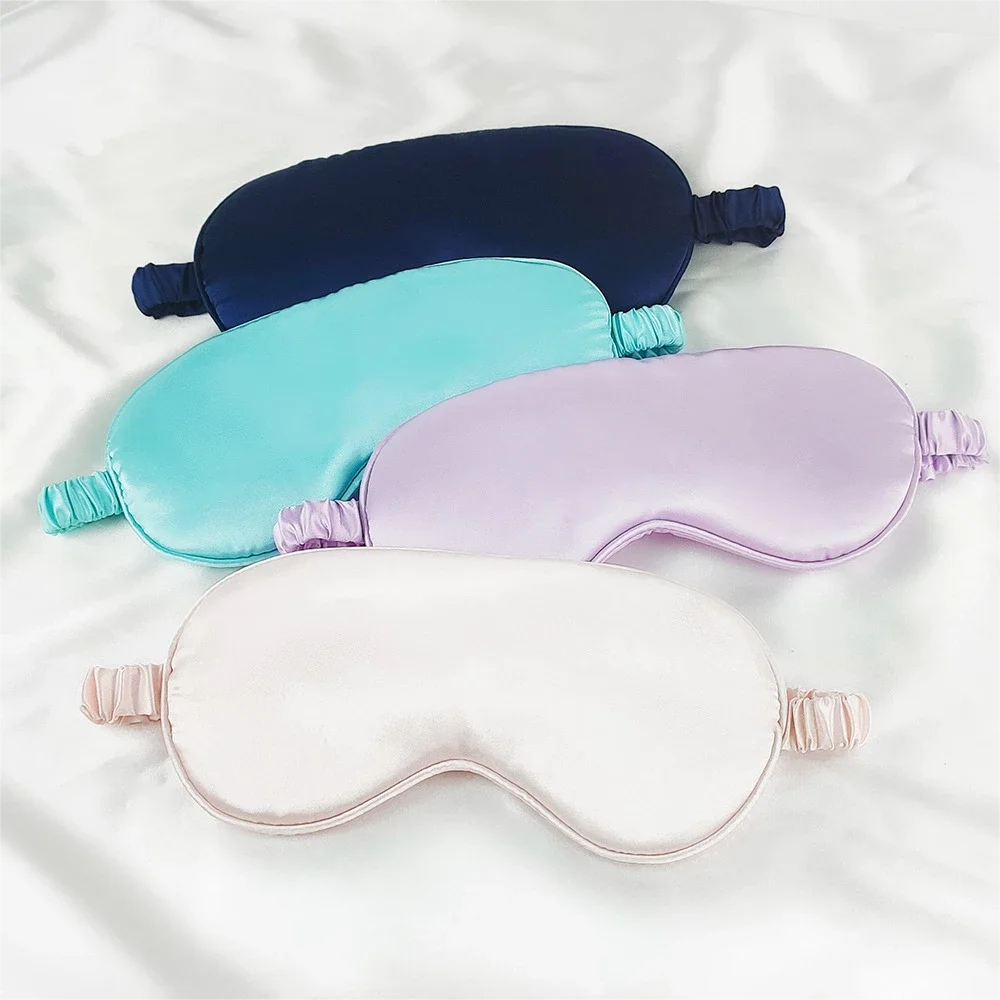 Three colored silk sleep masks in navy blue, turquoise, and lavender laid on a white surface.