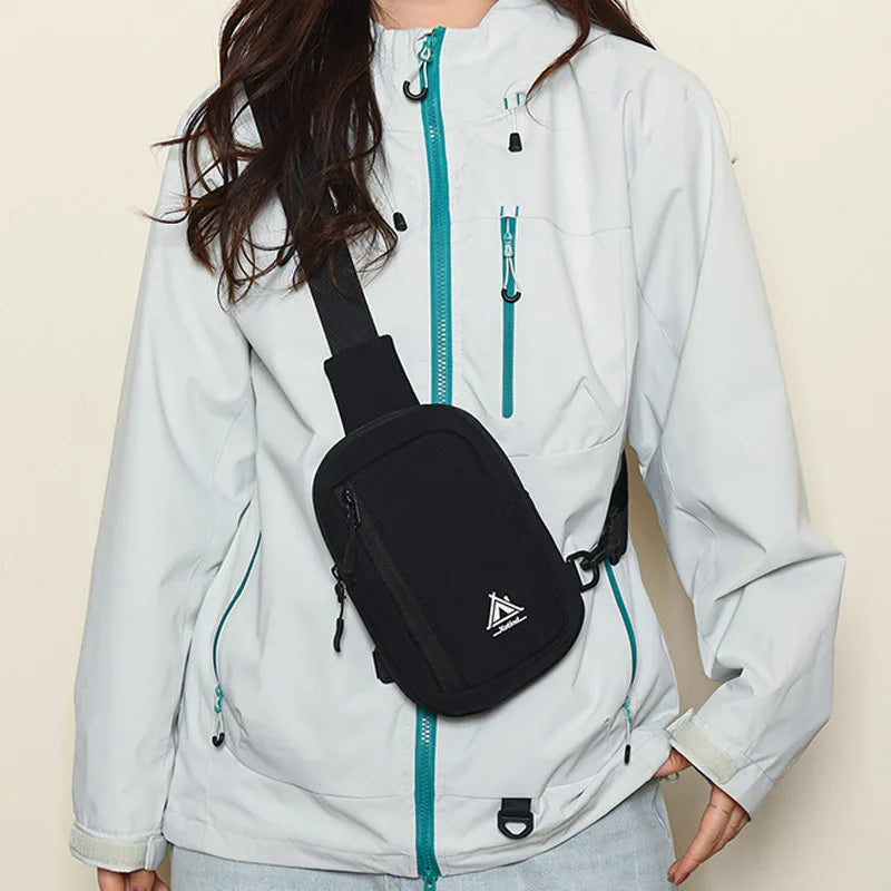 A woman is wearing a light gray jacket with a black sling bag attached to the front zipper.