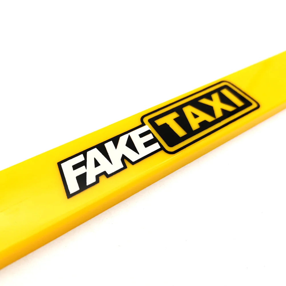 A yellow license plate frame with black text reading FAKE TAXI, shown diagonally.