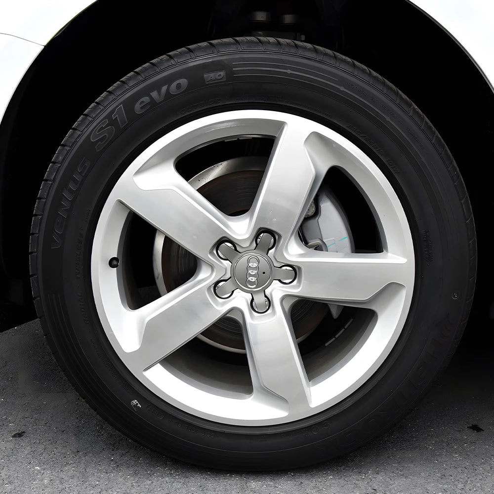 Silver Audi wheel with tire mounted on a black vehicle.