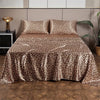 Luxury satin leopard print bedding set displayed on a bed with modern headboard and dark wood floor.