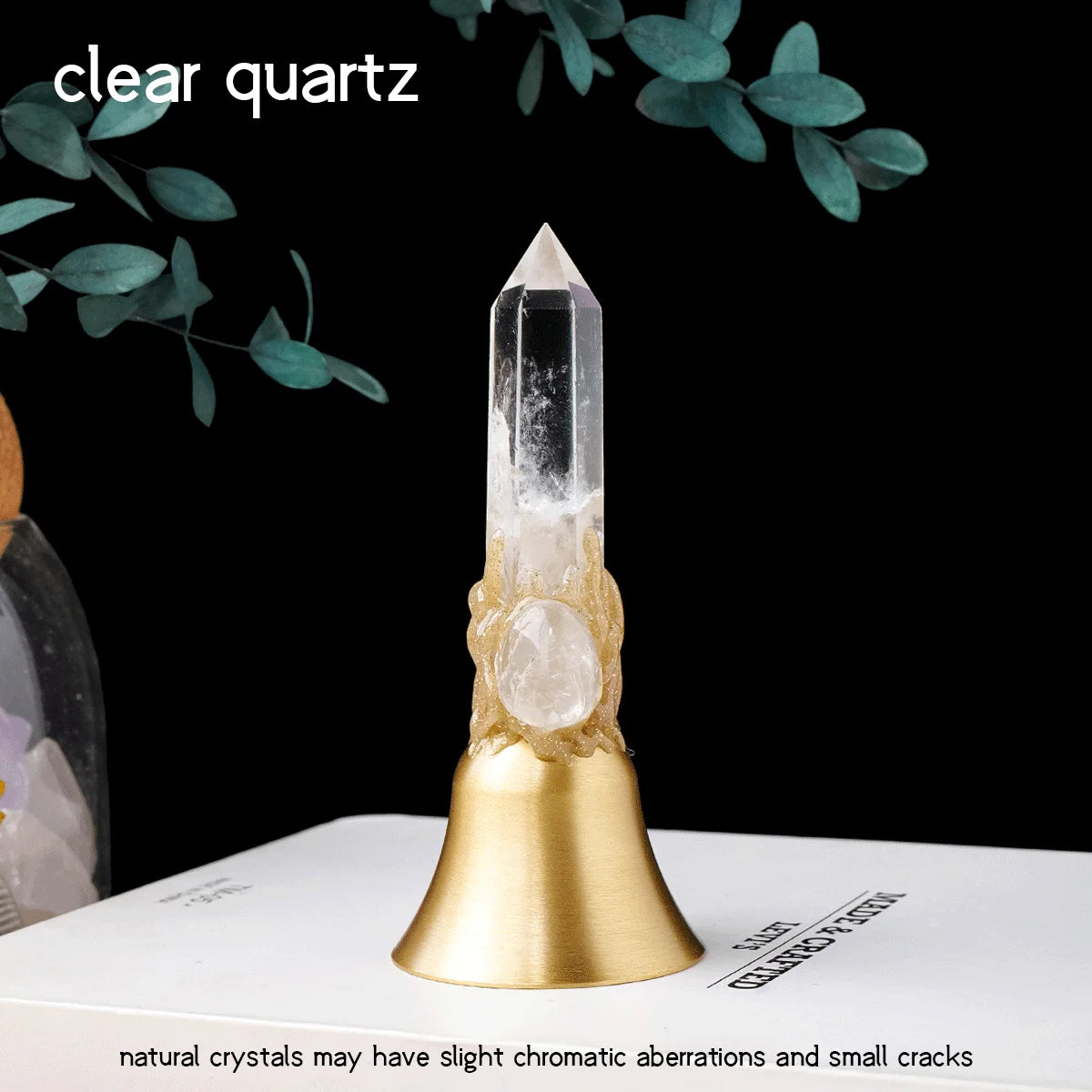 A clear quartz point crystal mounted on a brass bell, set against a dark background.