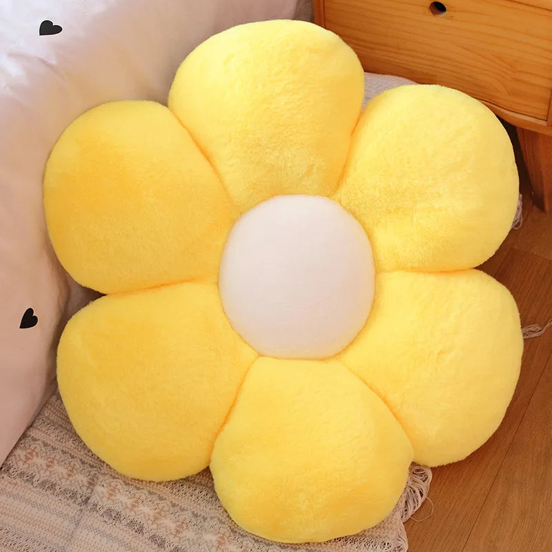 A bright yellow sunflower shaped plush pillow with a white center, resting on a light fabric.
