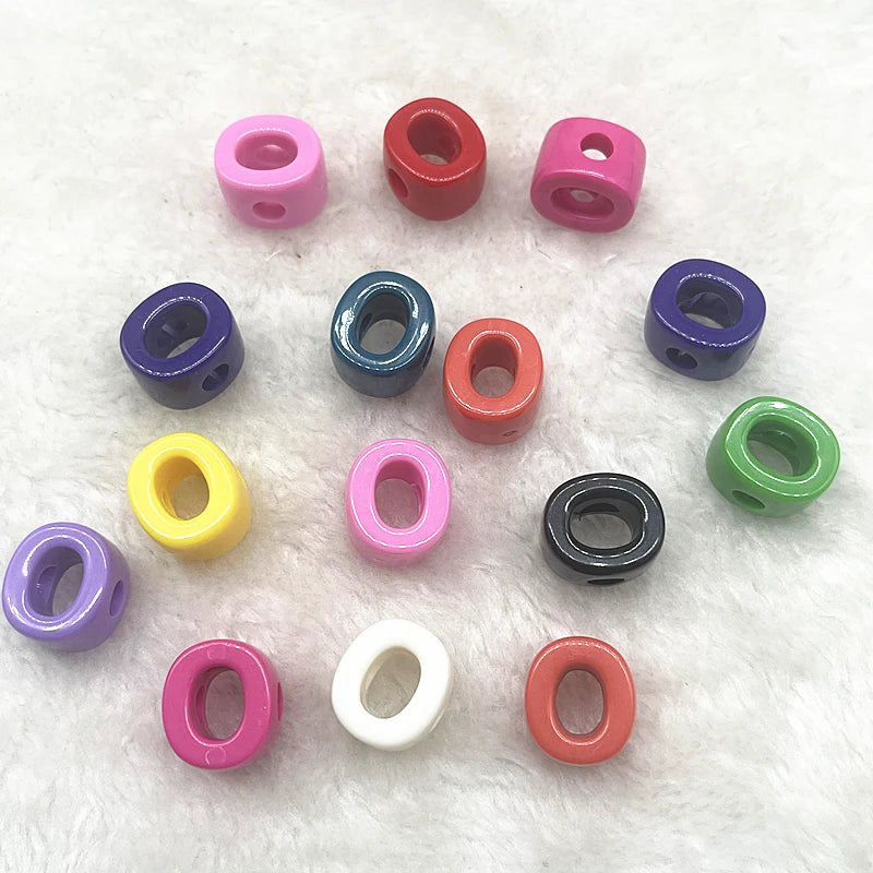 A collection of ten mixed colored letter beads in various shapes and sizes laid out on white fluffy material.