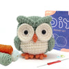 A handmade crocheted owl toy in green and cream colors next to yarn and a crochet needle.
