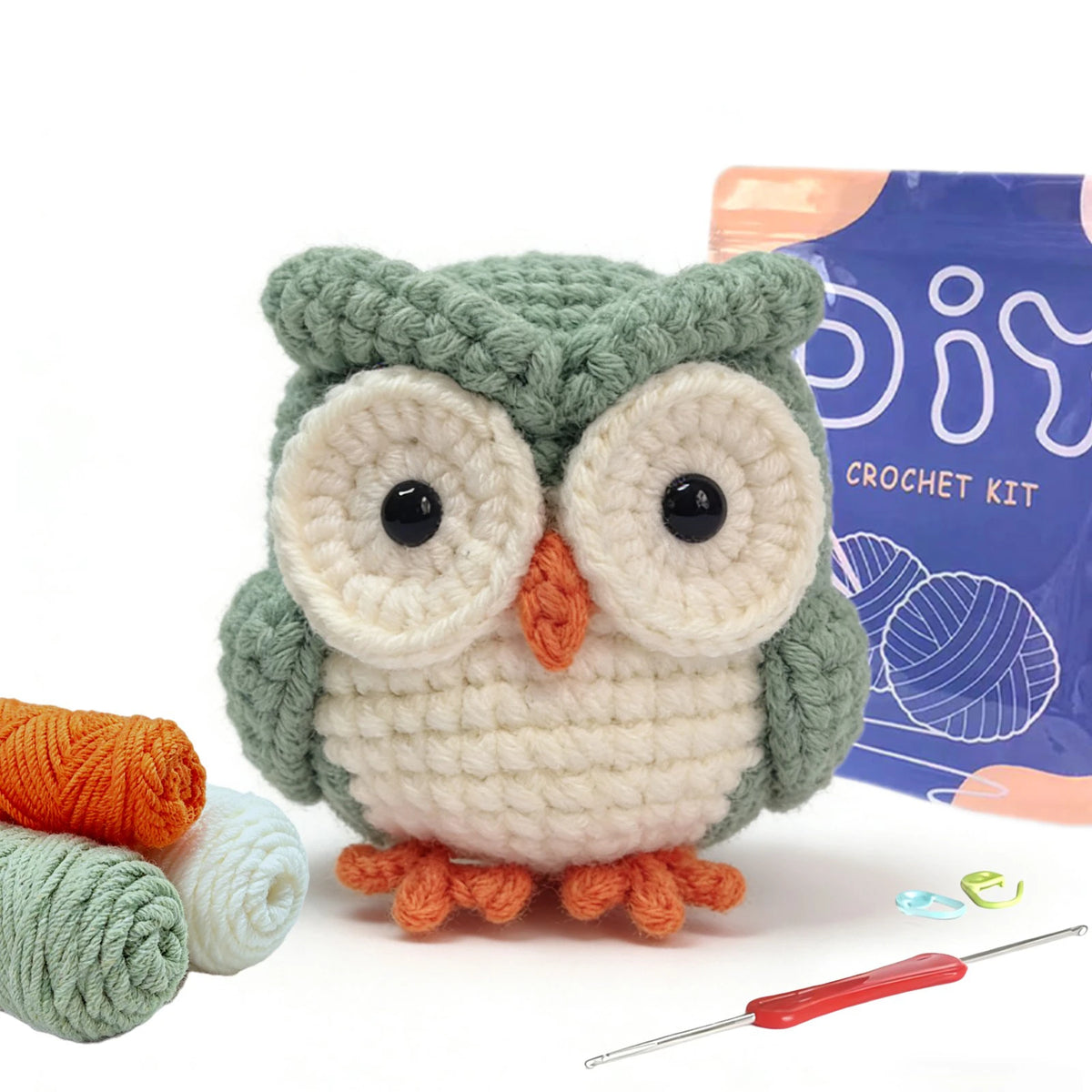 A handmade crocheted owl toy in green and cream colors next to yarn and a crochet needle.