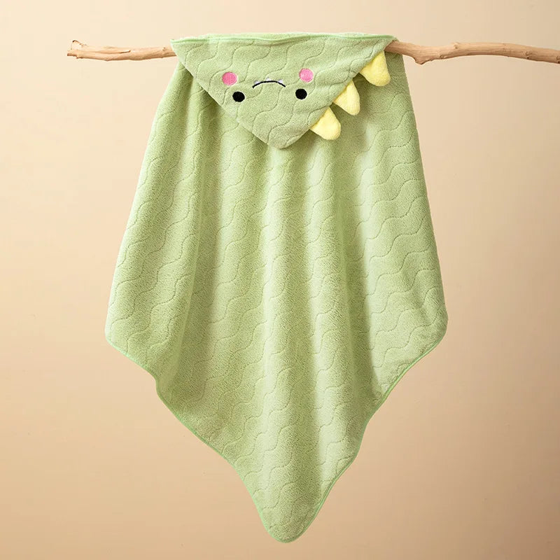 A light green hooded baby bathrobe towel with a cartoon dragon face design hanging on a wooden branch.