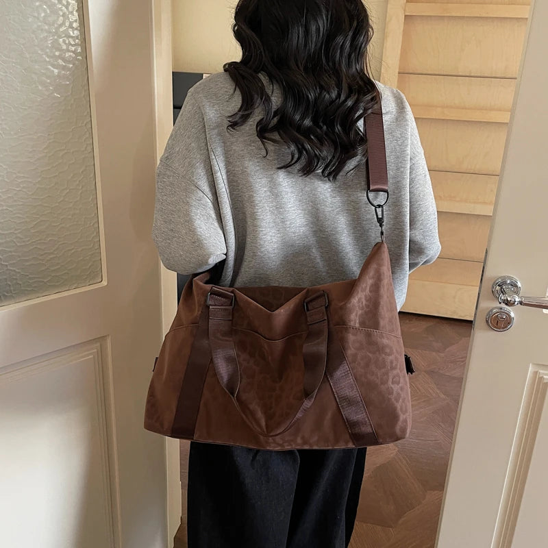 A woman is holding a brown leopard print duffle bag with an adjustable strap in a hallway.
