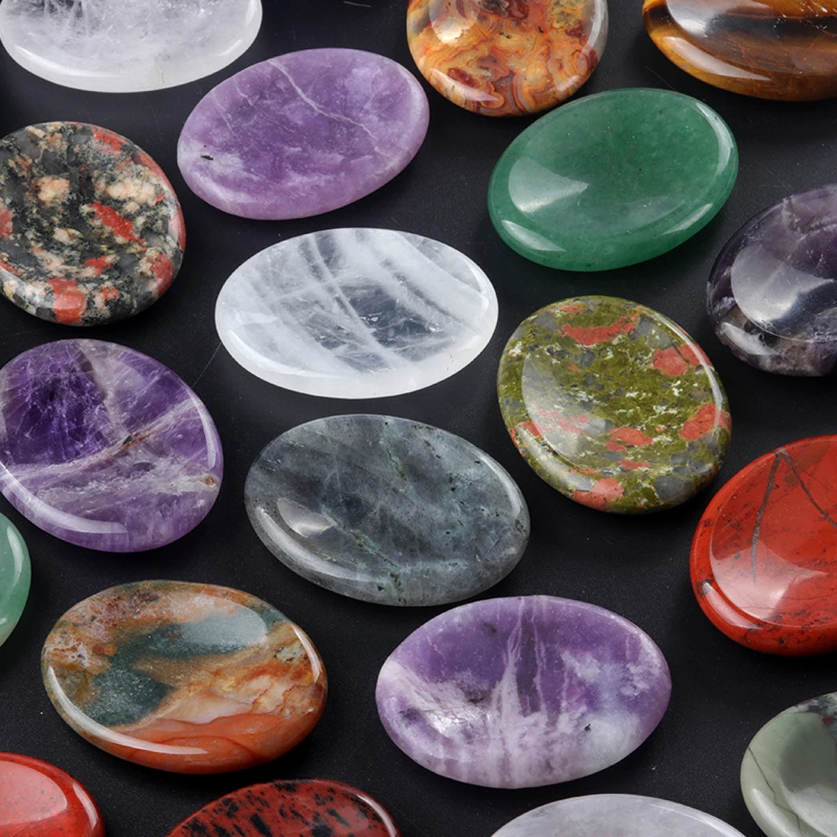 A collection of oval natural crystal stones in various colors including purple, green, orange, and gray.