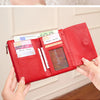 A close-up of a red leather tri-fold wallet with a zipper and coin pocket being held by a hand.
