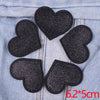 A set of five black glitter heart iron-on embroidered patches placed on a light blue denim fabric.