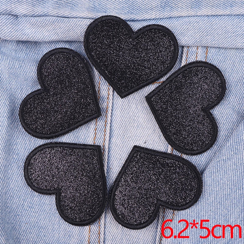 A set of five black glitter heart iron-on embroidered patches placed on a light blue denim fabric.