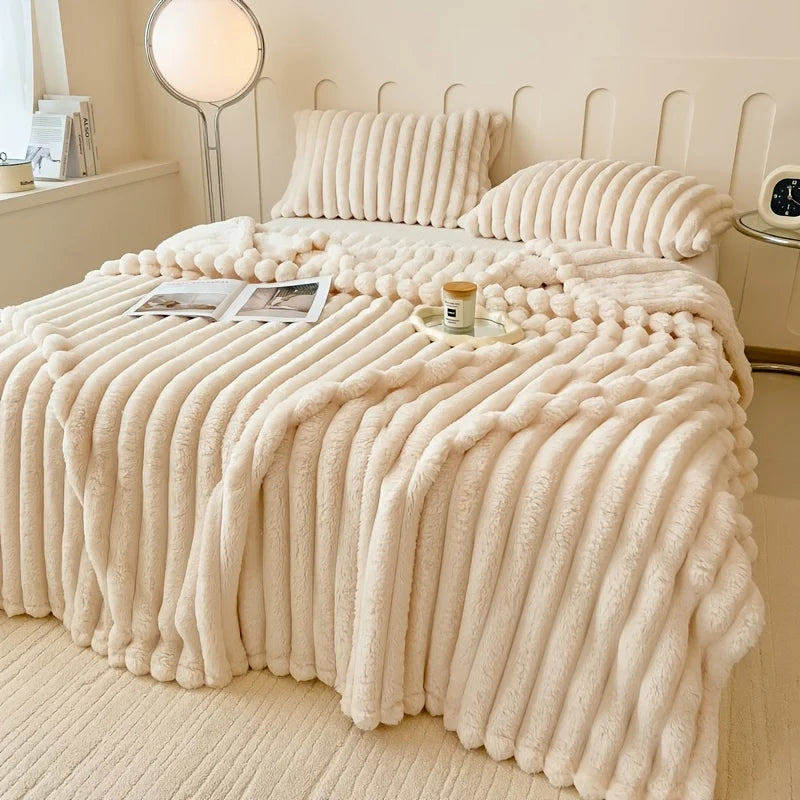 A thick, cream-colored flannel blanket with vertical ribbing is draped over a bed, featuring matching pillows and a nearby la
