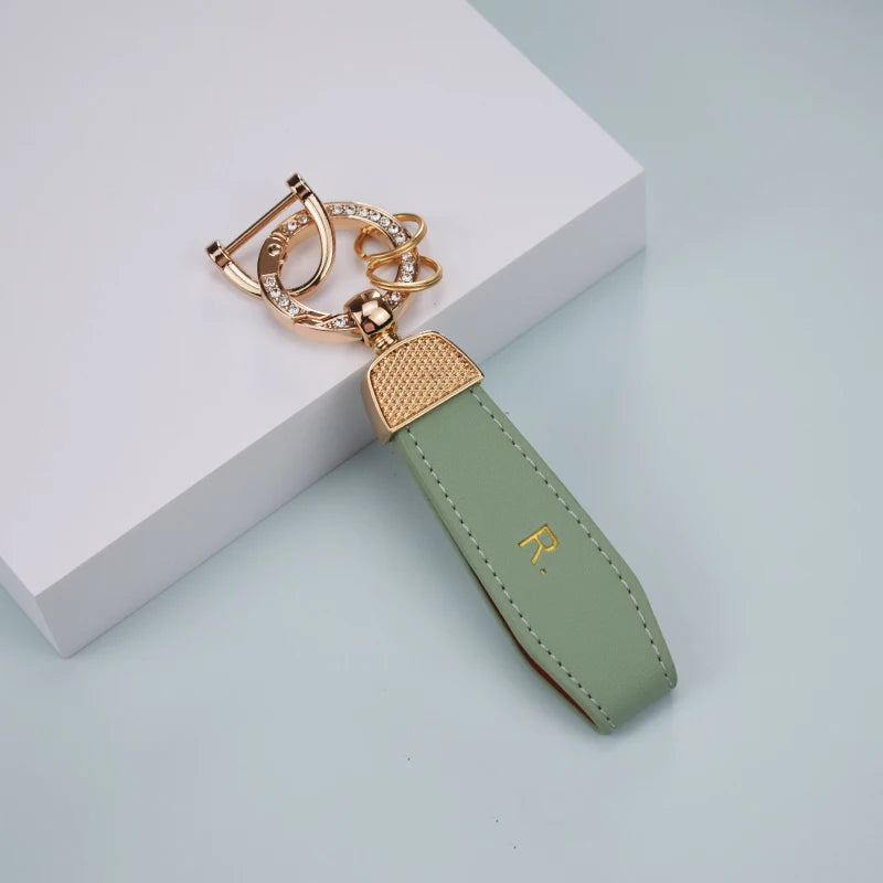 A gold-toned key fob with a leather cover and a protective TPU sleeve resting on a white surface.