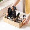 A hand holds a wooden box containing various gardening tools including tweezers, scissors, and a spray bottle.