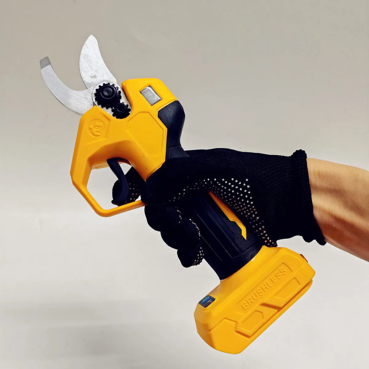 A hand holds a yellow cordless multi-blade cutting shear tool with a silver blade against a light background.