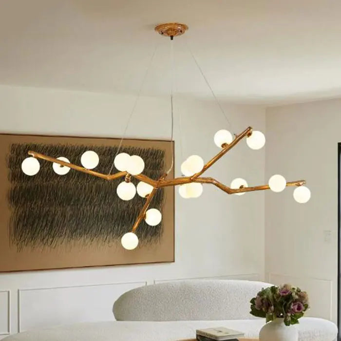A modern chandelier with a gold-toned branch structure and spherical frosted glass lampshades hanging in a bright room.
