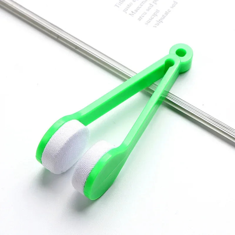 A bright green portable double-sided glasses cleaning brush with white microfiber pads resting on a white surface.