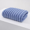 A rolled light blue plush bath towel with a textured surface is displayed on a white surface.