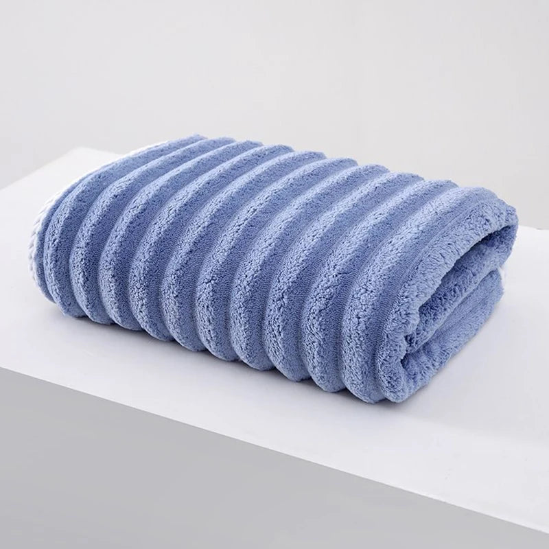A rolled light blue plush bath towel with a textured surface is displayed on a white surface.