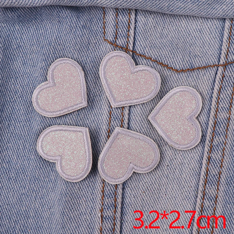 A set of five pink glitter heart iron-on embroidered patches placed on a denim fabric.