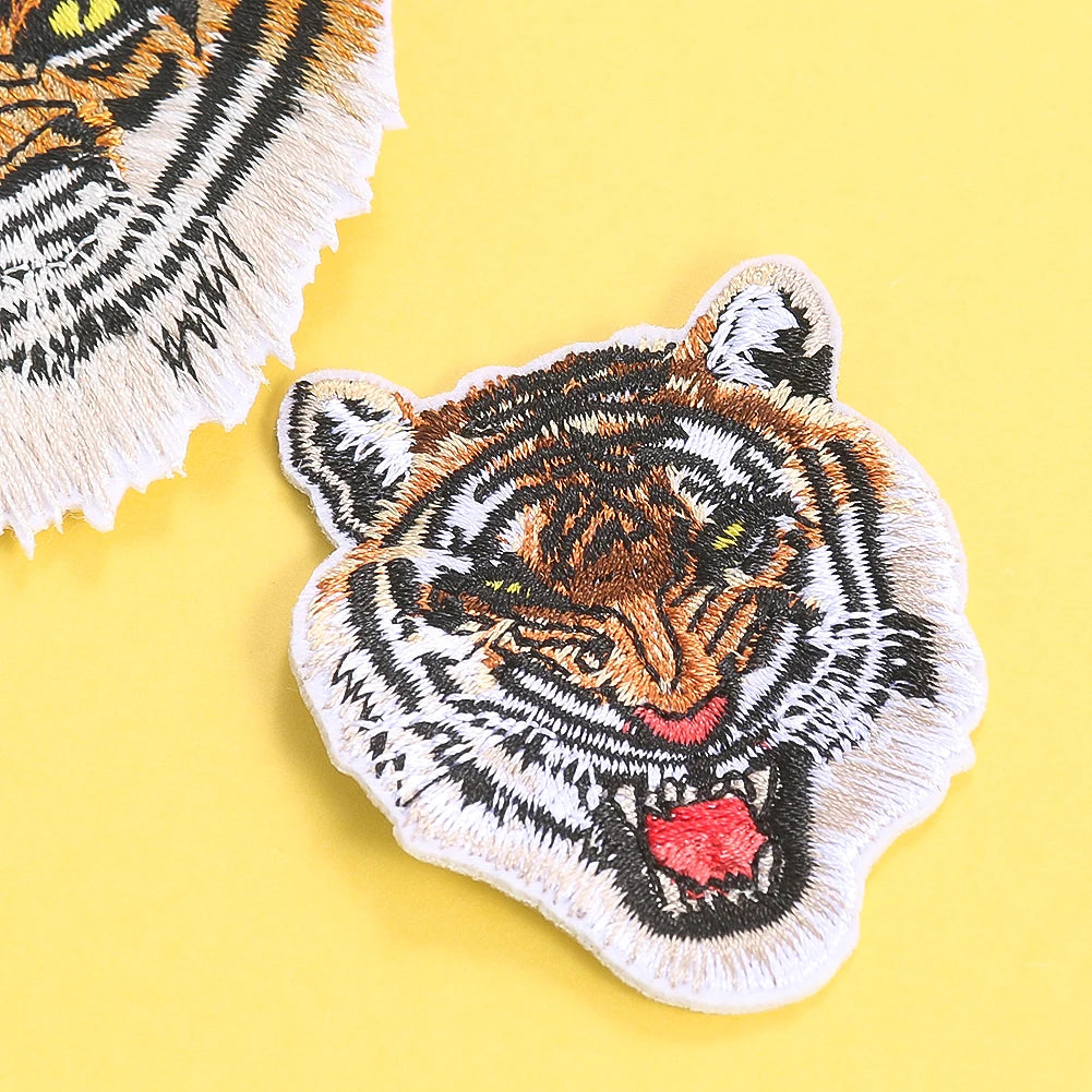 A detailed embroidery patch of a tiger head in black, orange, and white on a yellow background.