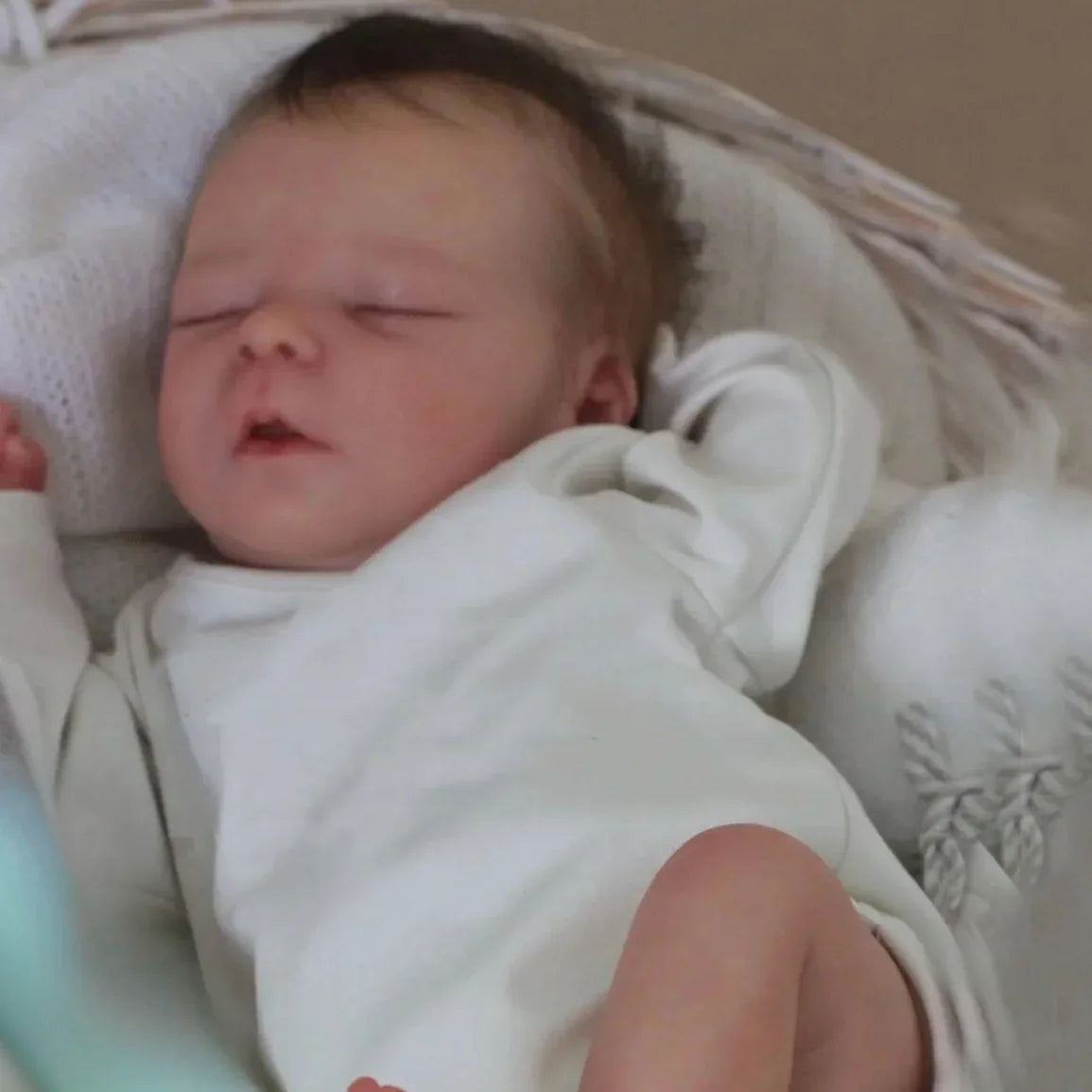 A newborn baby doll with painted veins and a soft cloth body is sleeping in a white blanket.