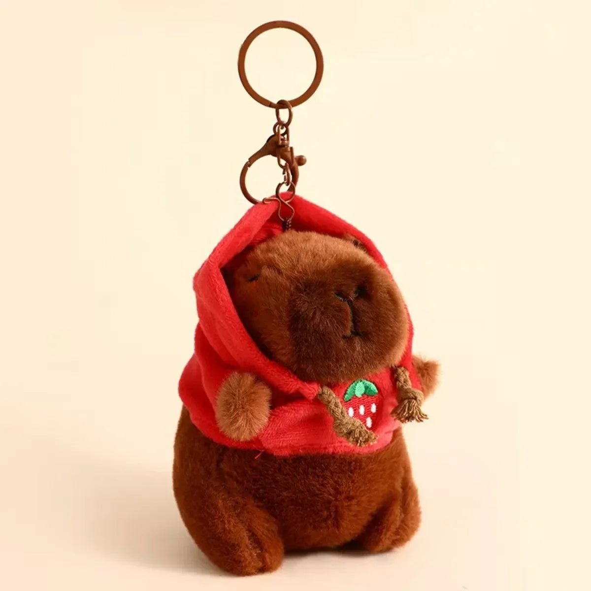A brown capybara plush toy with a red hood and a gold-colored keychain ring.
