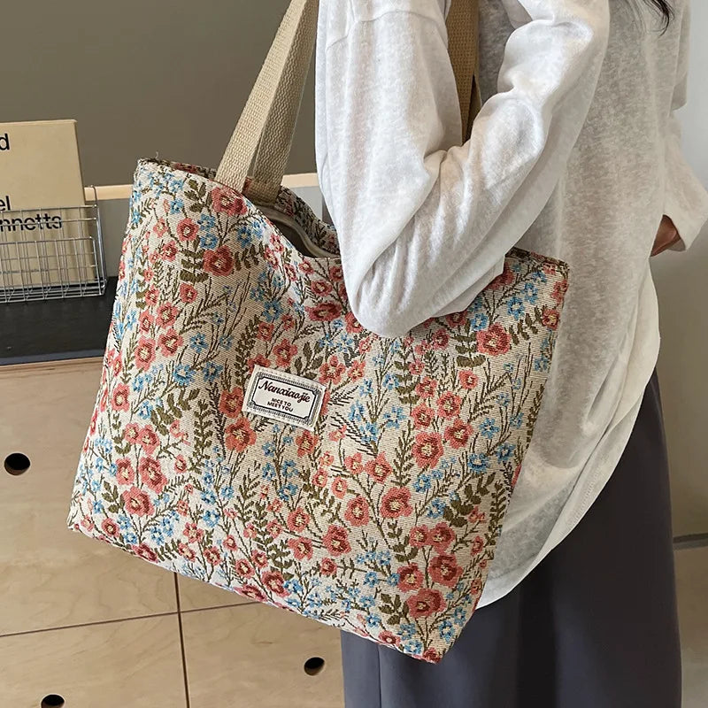 A person holds a beige corduroy tote bag with floral accents against a light background.