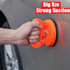A hand is using an orange suction cup tool to pull a dent from a car body panel.