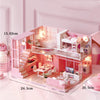 A pink wooden dollhouse miniature building kit featuring furniture and interior details.
